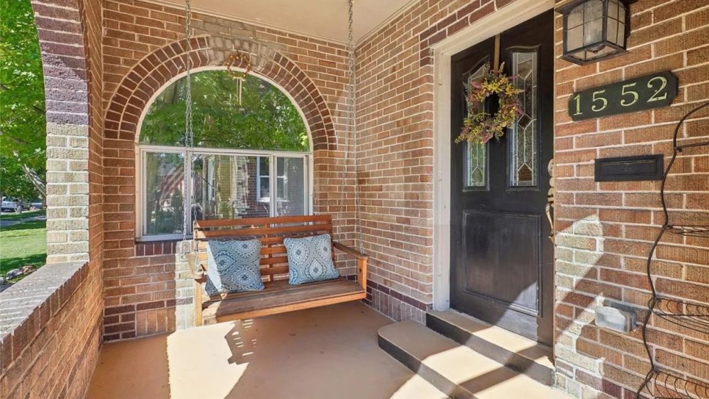 Cozy brick porch with swing and arched window.