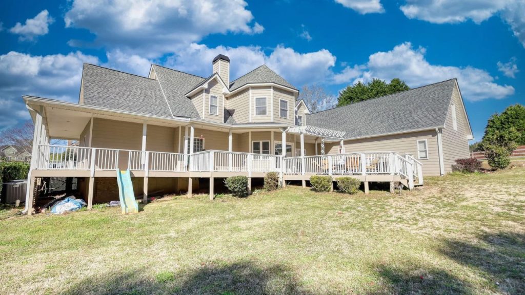 Cozy porch wraps around a house with charming rooflines and a sunny backyard.
