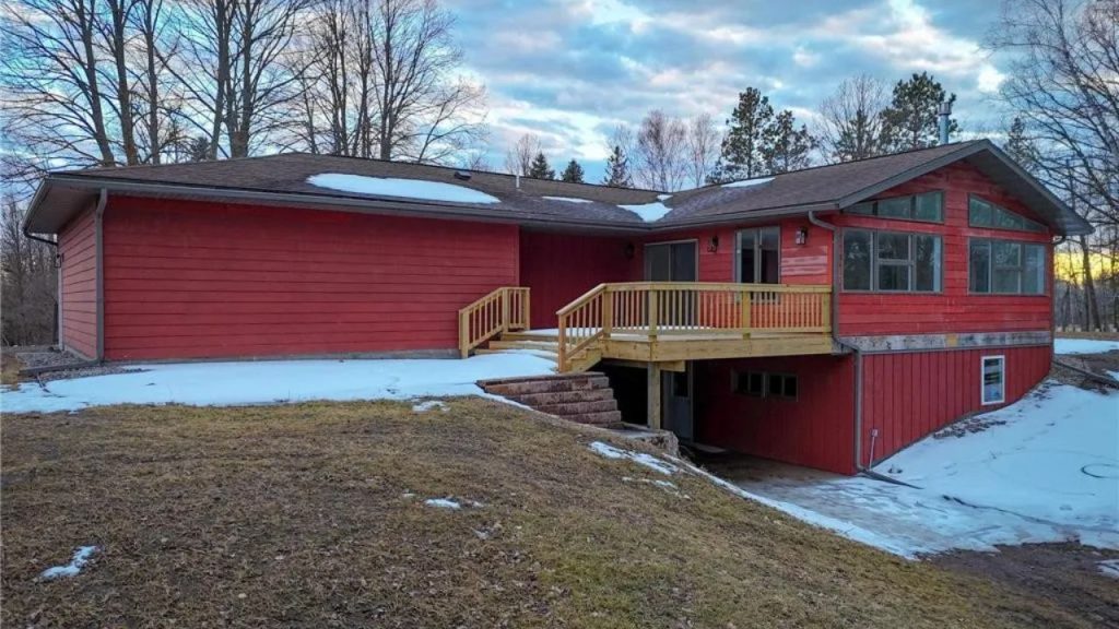 Red ranch home with walkout basement, wooden deck, and snowy yard.