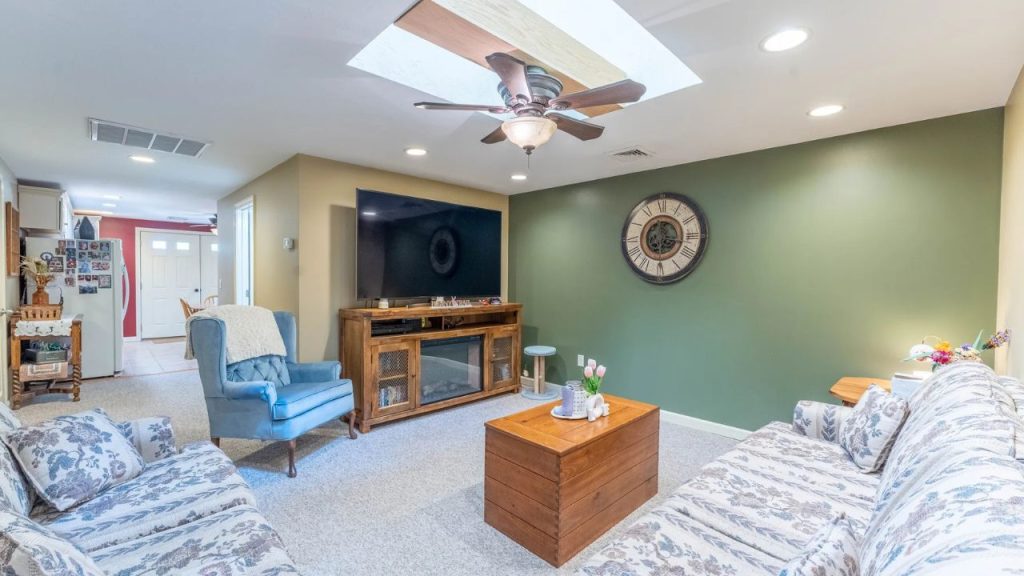 Cozy living room with a sage-green accent wall, wooden furniture, and floral-patterned seating.