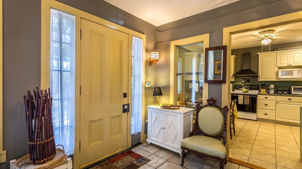 Entryway with yellow door, antique chair, and a view into a traditional kitchen.