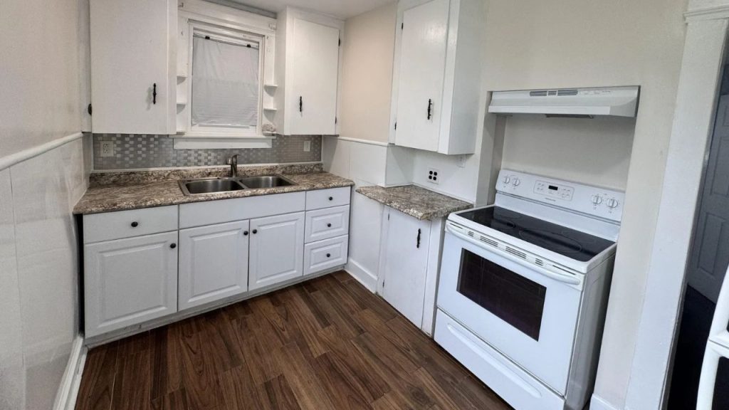 A bright kitchen with wooden floors, white cabinets, a granite countertop, and a modern stove.