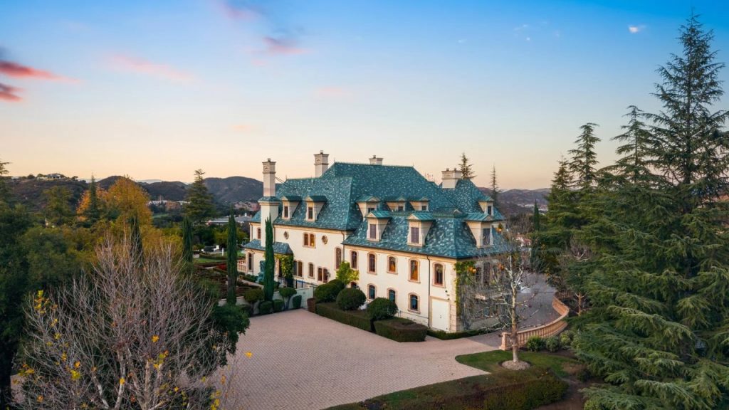 A stunning hillside mansion with teal roofs, surrounded by trees and rolling hills at sunset.