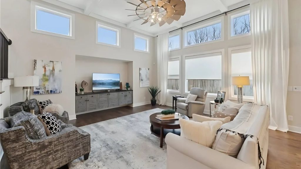A bright living room with high ceilings, a windmill chandelier, and cozy furniture near large windows.