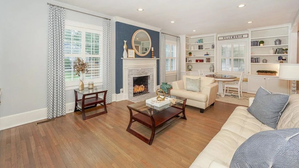 A cozy living room with cream sofas, a blue accent wall, fireplace, and built-in shelves under large windows.