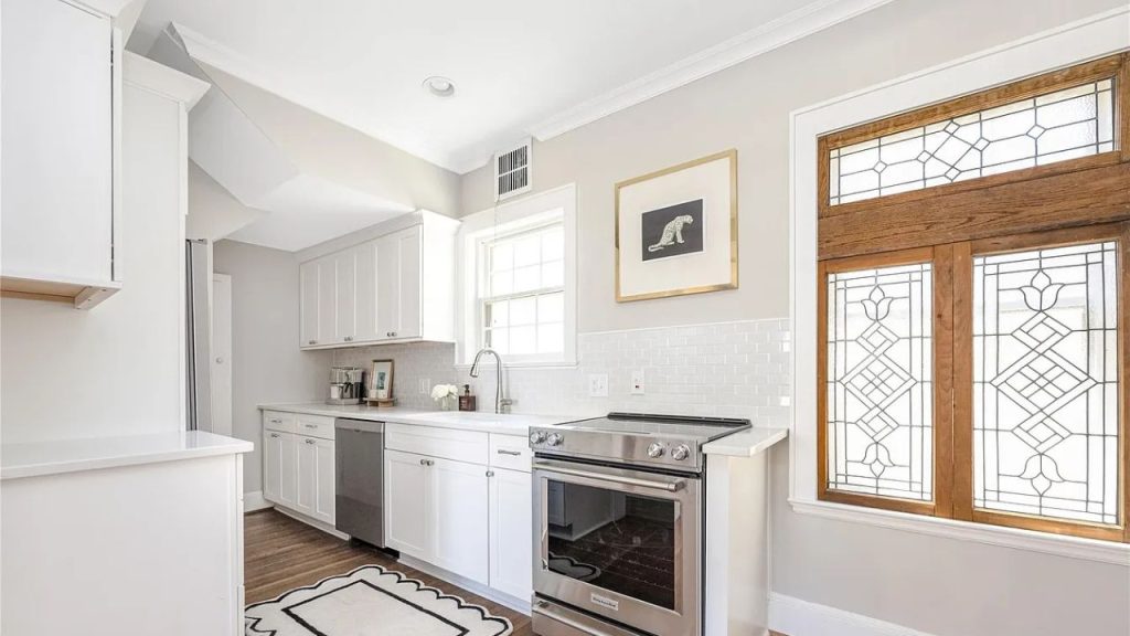 A bright kitchen with stained-glass windows, white cabinets, and a stainless-steel oven.