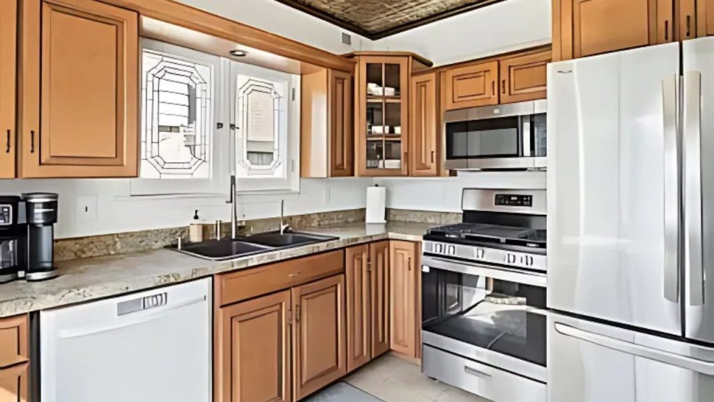 A warm kitchen with wooden cabinets, stainless steel appliances, and large decorative windows.