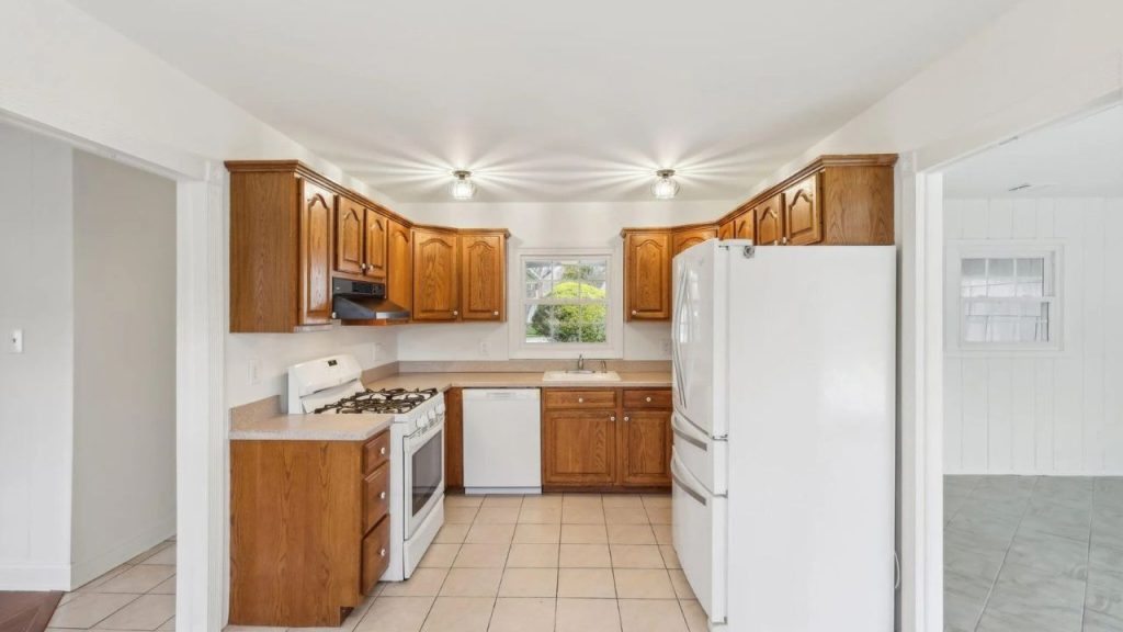 A cozy kitchen with wooden cabinets, white appliances, and a bright window, bathed in soft lighting.