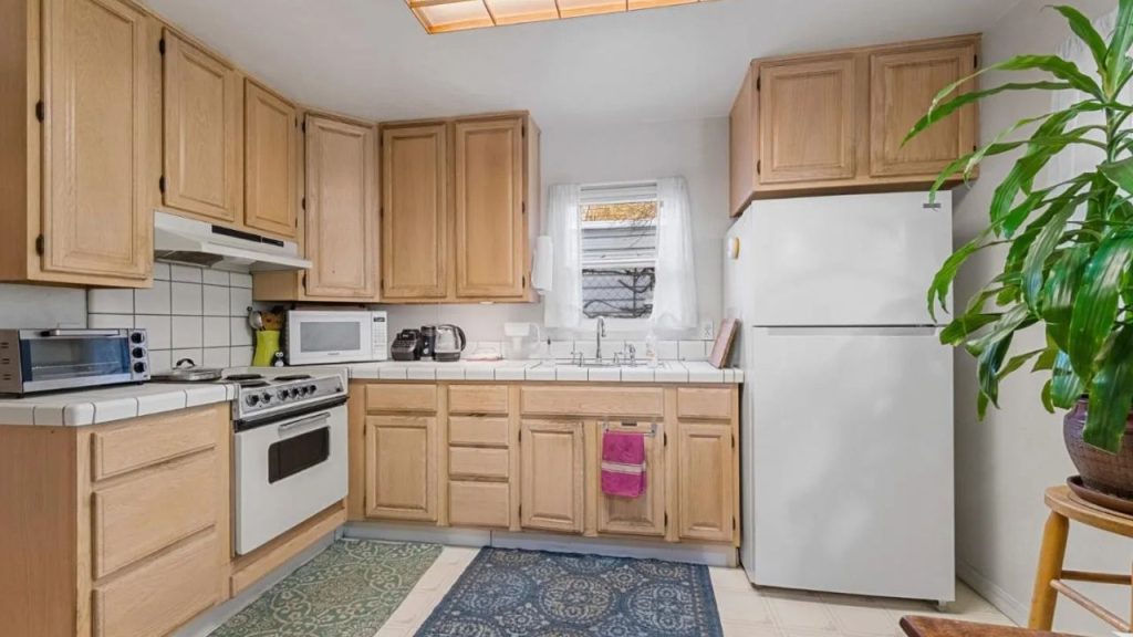 A homely kitchen with wooden cabinets, white appliances, and a blue rug.