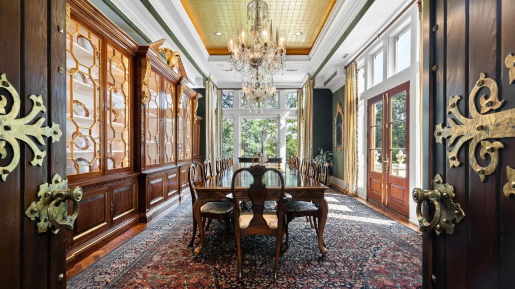 An opulent dining room with a grand chandelier, elegant wood furniture, and large windows opening to a scenic view.