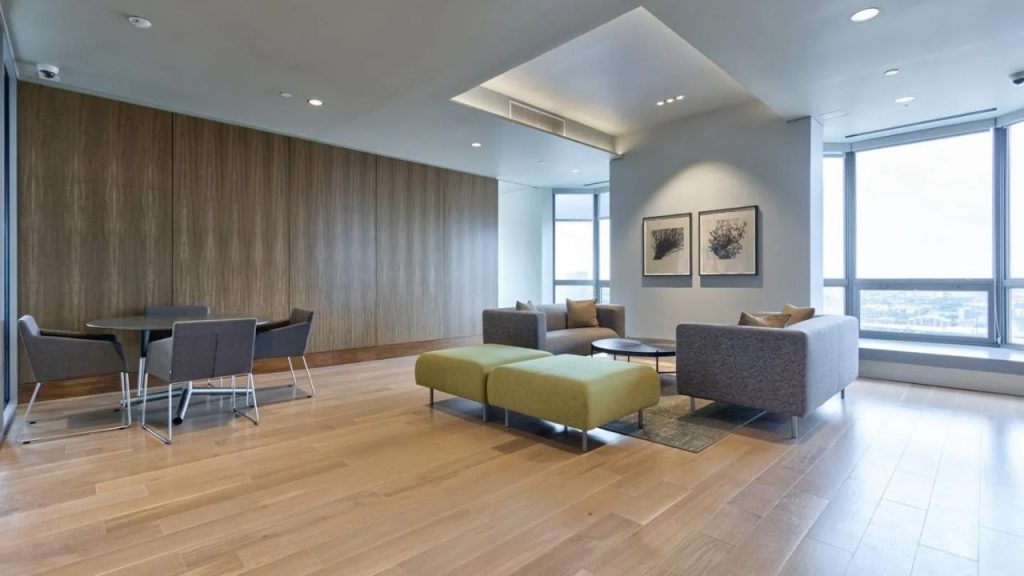 Modern lounge with gray sofas, green ottomans, and large windows overlooking the city.