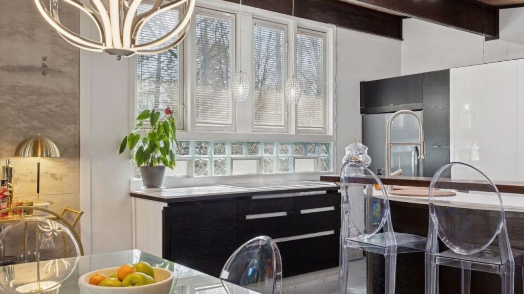 Bright modern kitchen with dark cabinets, pendant lights, and clear chairs.