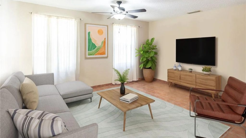A bright living room with a gray sofa, wooden coffee table, potted plant, TV console, and abstract art.