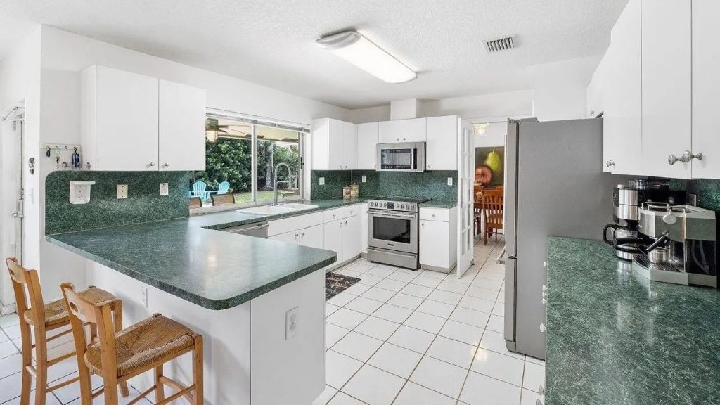 A bright kitchen with white cabinets, green counters, and a cozy breakfast bar.