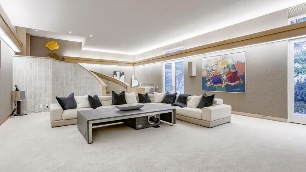 Modern living room with curved staircase, plush sectional, and abstract wall art.