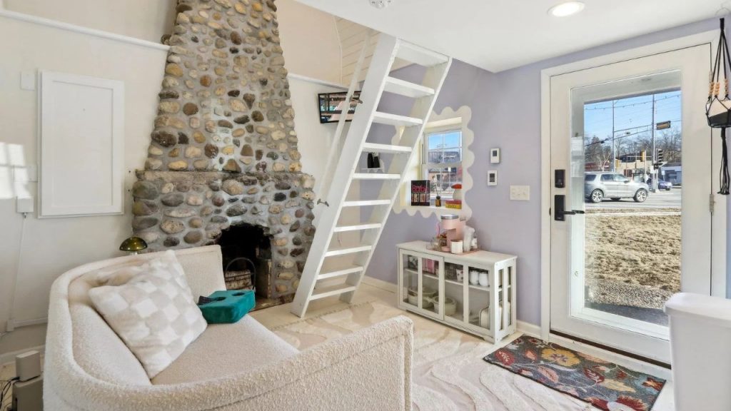 Cozy living area with a stone fireplace, loft ladder, and soft-toned decor.