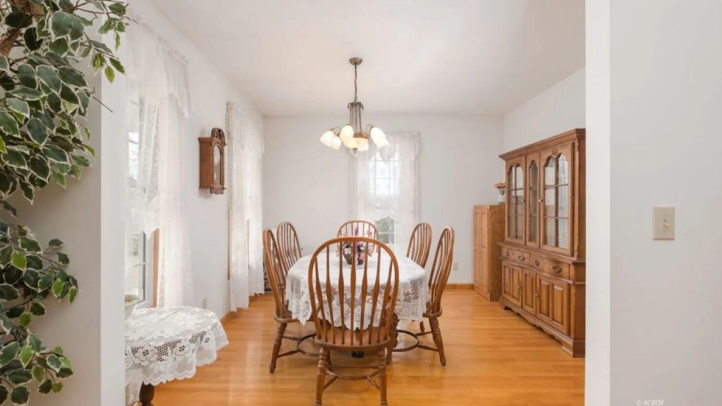 Bright dining room with lace curtains, wooden furniture, and a classic chandelier.