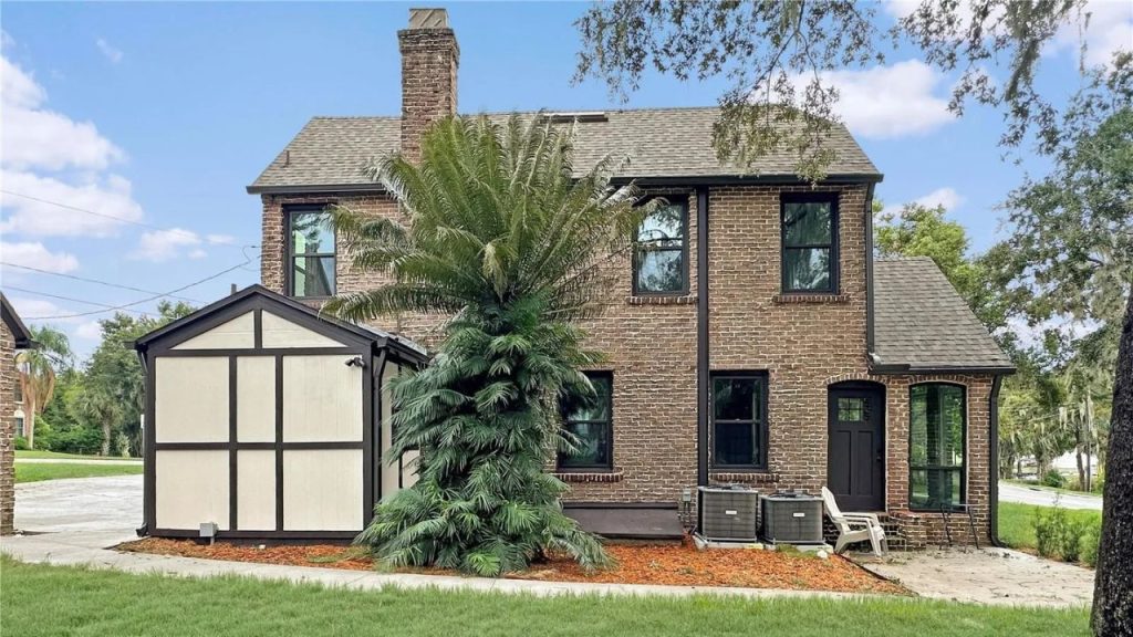 Back view of a brick Tudor home with a palm tree and bay window.