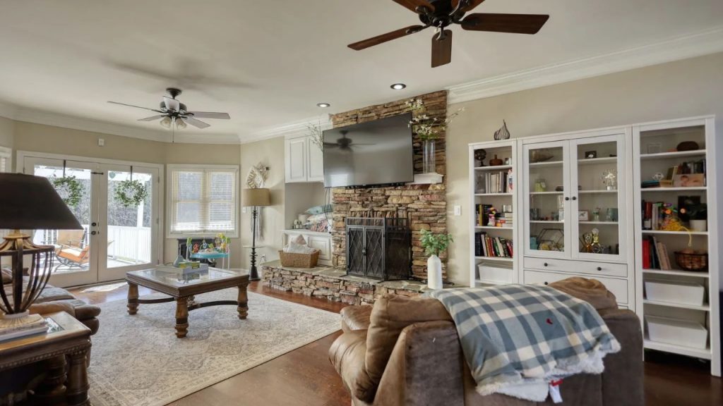 Warm living room with stone fireplace, bookshelves, and natural light.