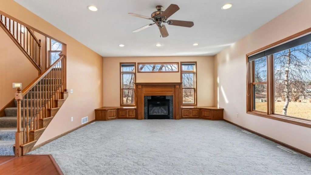 Carpeted living room with fireplace, wood trim, and large windows.
