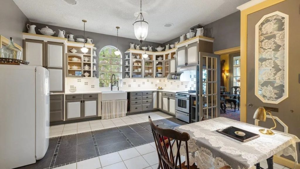 Vintage kitchen with open shelving, gray and cream cabinets, and a lace-covered breakfast table.