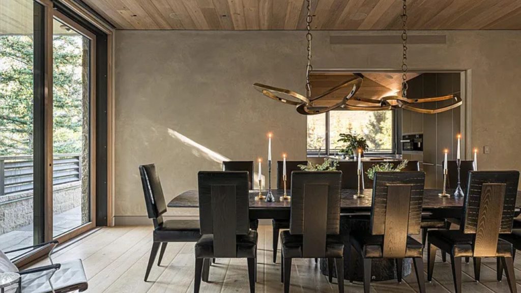 A stylish dining room with a wooden chandelier and views of trees outside.