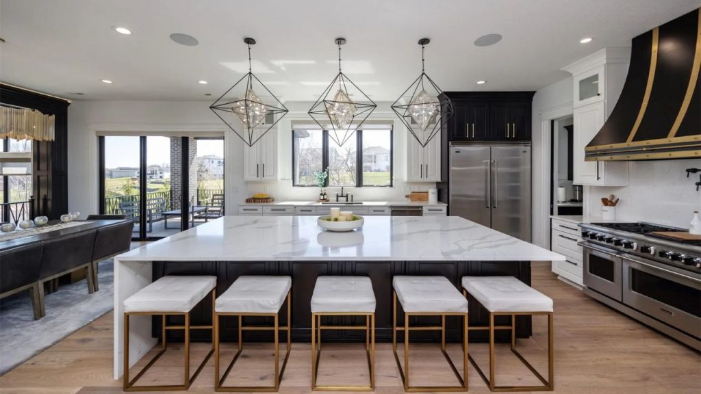 A sleek kitchen with a marble island, gold-framed stools, geometric pendant lights, and large windows, offering a bright and elegant vibe.