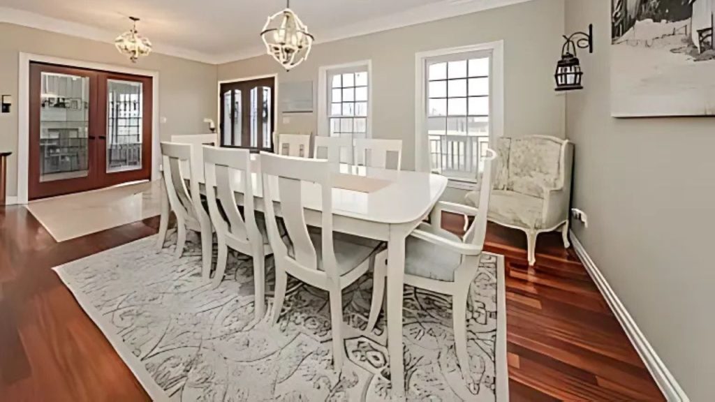 A stylish dining area with a white table, chandeliers, and large windows.