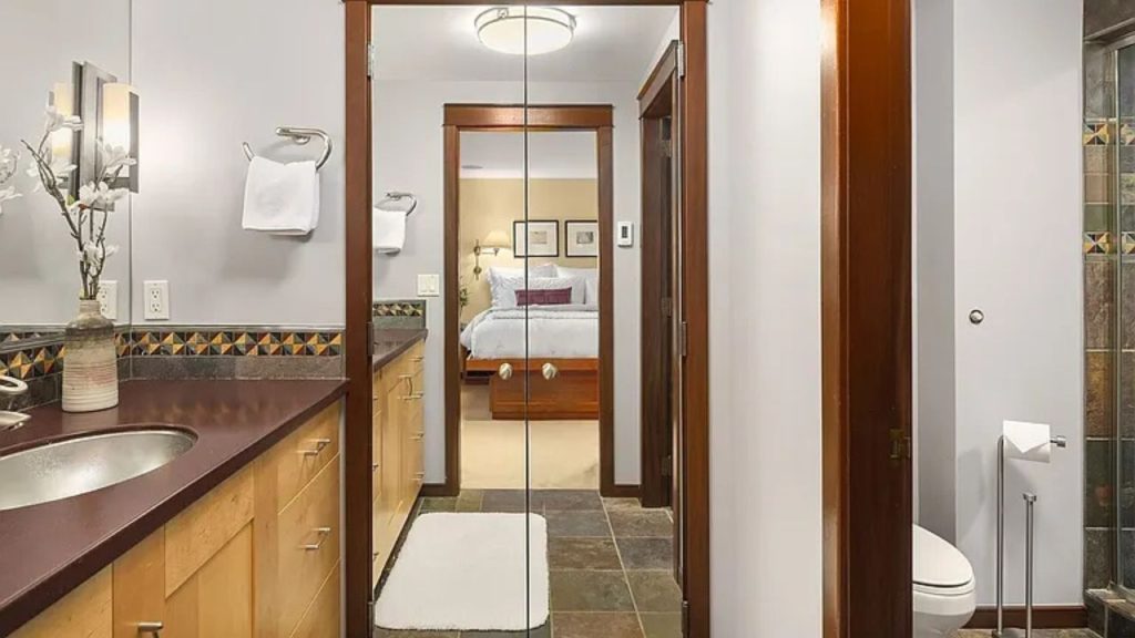 Warm-toned bathroom with slate flooring, wood cabinetry, and glass doors to bedroom.