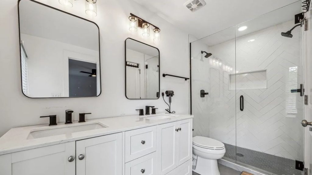 A modern bathroom with dual sinks, a glass shower, and herringbone tile design.