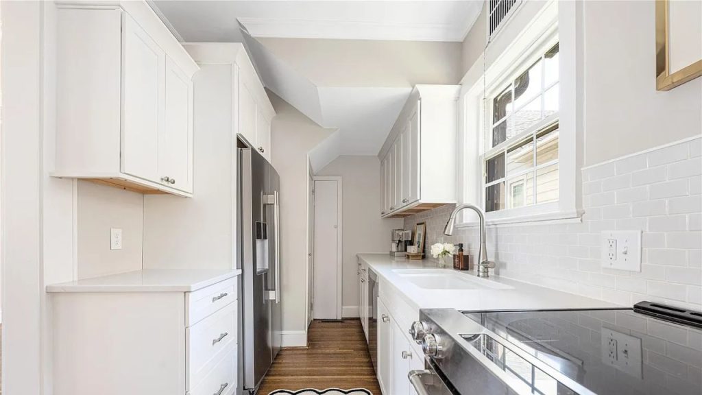 A bright kitchen with white cabinets, stainless-steel stove, and large windows.