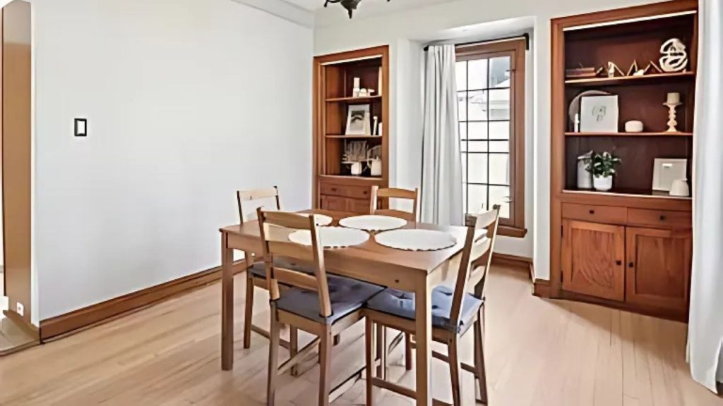 A bright dining area with a wooden table, chairs, and built-in shelves by large windows.