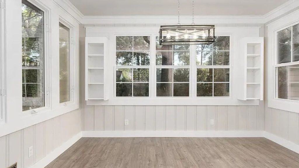 A sunlit dining room with large windows, a chandelier, hardwood floors, and built-in shelves.