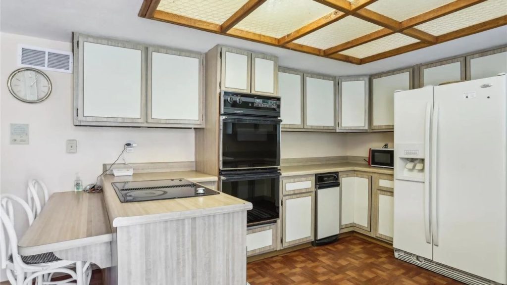 A warm kitchen with light wooden cabinets, double oven, breakfast bar, and parquet floor, featuring a wooden grid ceiling and modern appliances.