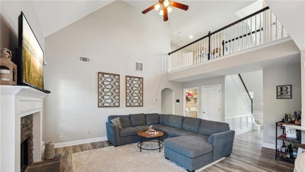 A spacious living room with a high ceiling, sectional sofa, fireplace, and loft overlook.