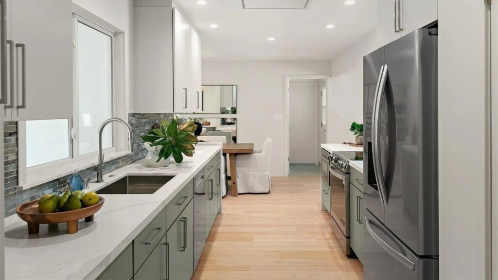 A bright kitchen with green cabinets, white marble counters, and modern appliances, featuring a dining area.