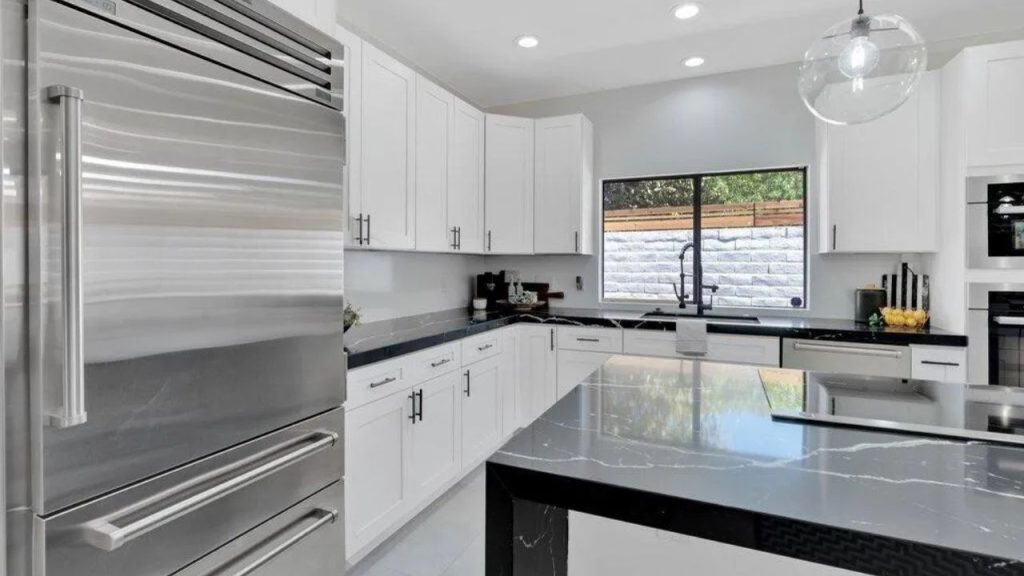 A modern kitchen with white cabinets, black marble counter, and a large stainless steel fridge.