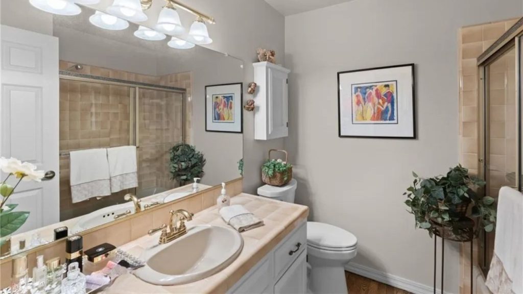A serene bathroom with gray walls, a beige-tiled shower, a vanity with plants, and colorful artwork.