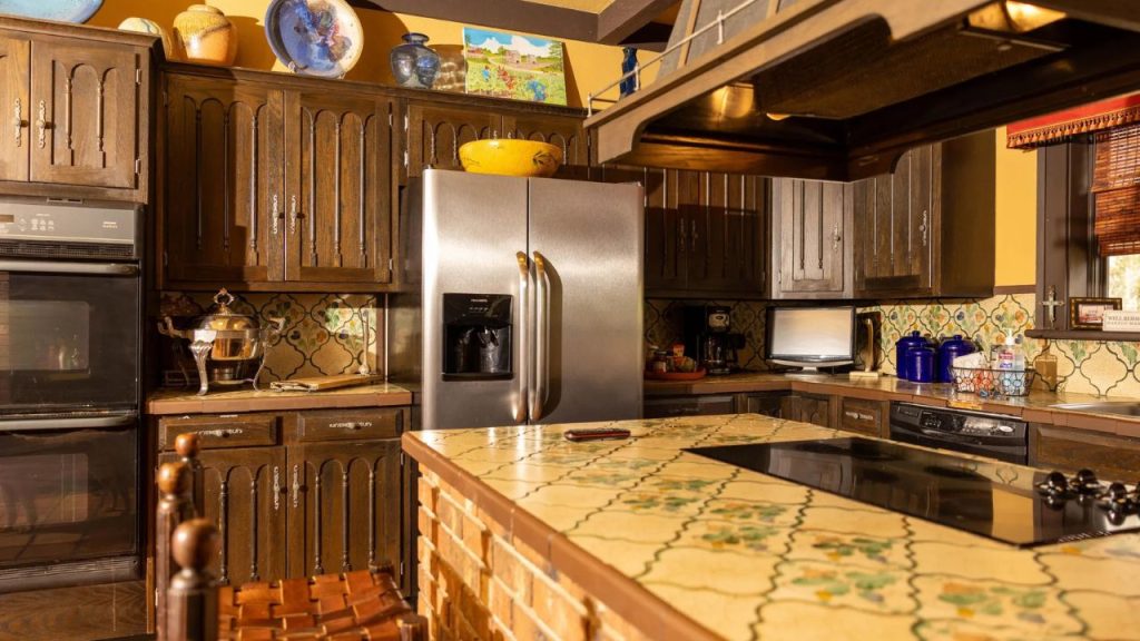Rustic kitchen with dark wood cabinets, tiled countertops, and a brick-accented island.