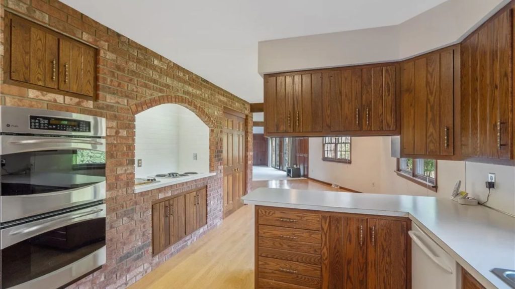 Brick-accent kitchen wall with arched cooktop and built-in ovens.