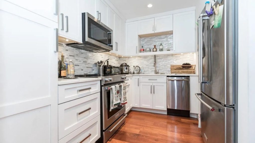 Small modern kitchen with white cabinets, stainless steel appliances, and wood floors.