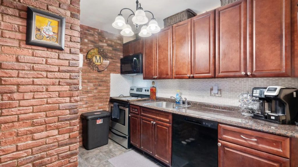Cozy kitchen with brick walls, cherry cabinets, and black appliances.