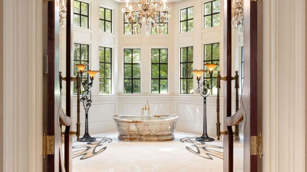 Luxurious bathroom with a stone tub, tall windows, and elegant lighting.
