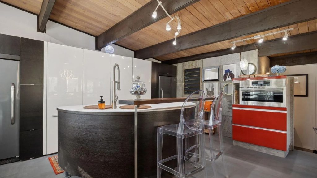 Stylish kitchen with red accents, wood ceiling, and clear barstools.