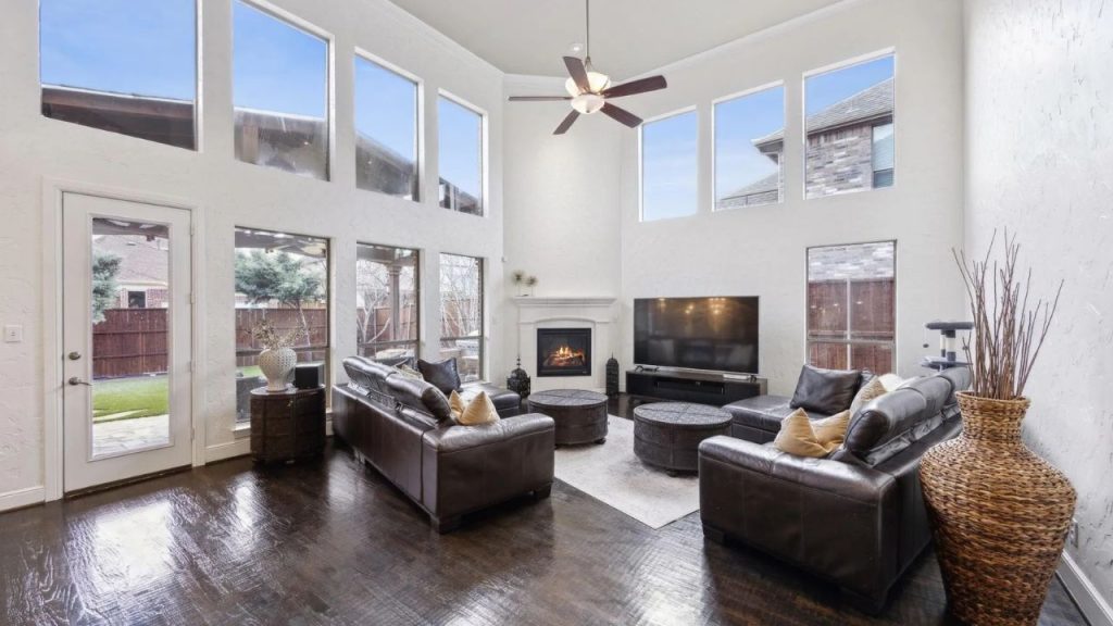 Spacious living room with tall windows, dark wood floors, and leather seating around a fireplace.