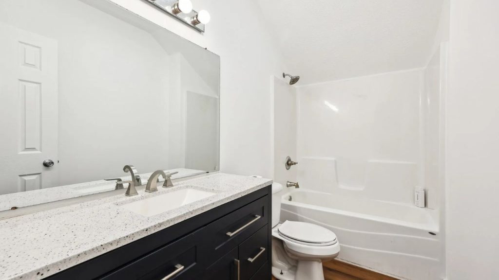 Modern bathroom with dark vanity, white countertop, and tub-shower combo.