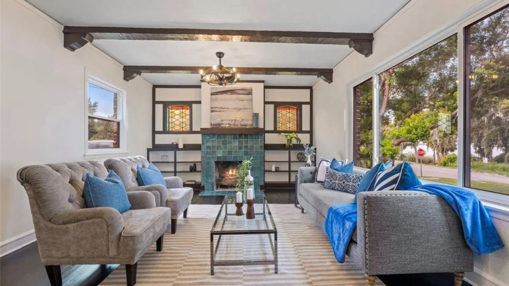 Living room with teal fireplace, wood beams, and large windows.
