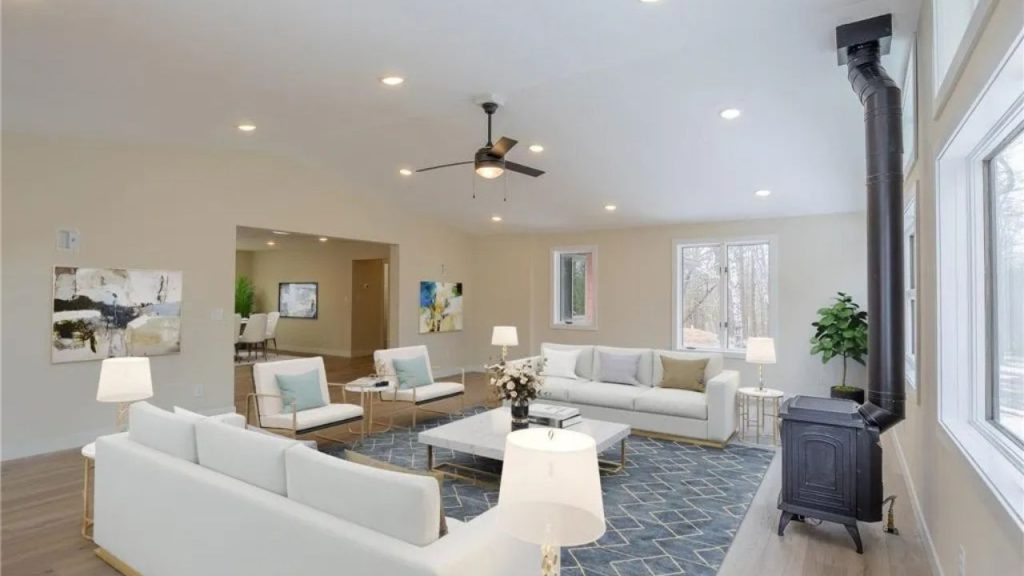 Bright living room with white sofas, blue rug, and black wood stove.