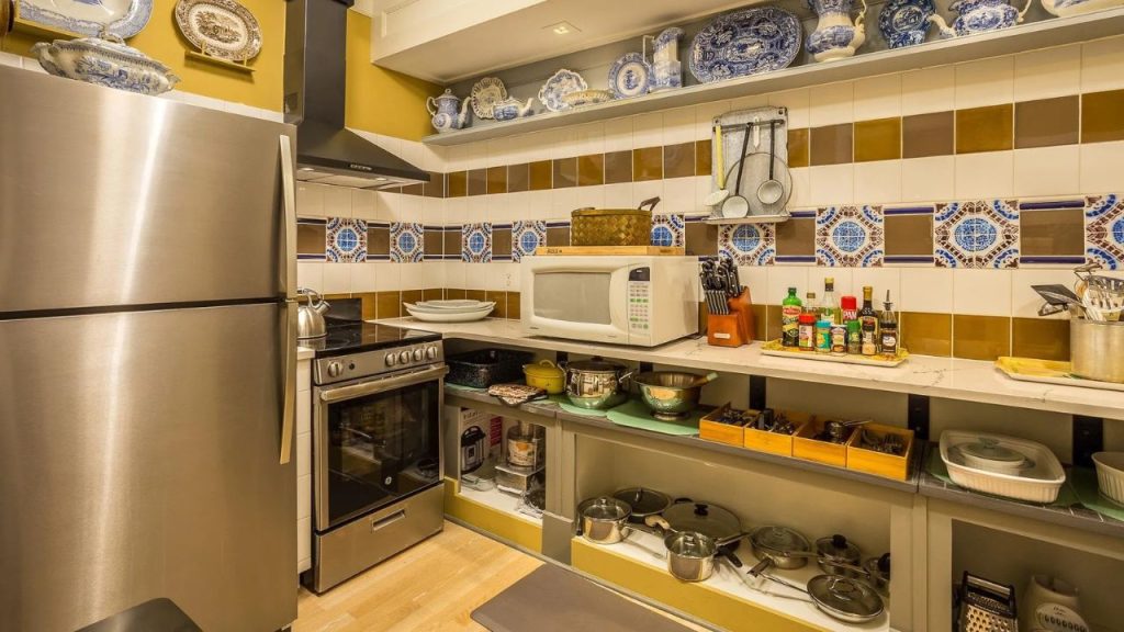 Warm kitchen with colorful tiled backsplash, open shelving, and blue and white dishware.