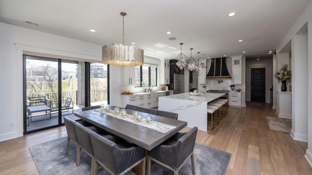 A bright kitchen and dining area with a marble island, pendant lights, and glass doors opening to a patio, exuding warmth and style.